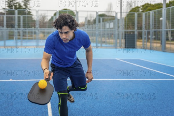 Male athlete concentrating while holding a pickleball paddle and yellow ball, ready to serve or