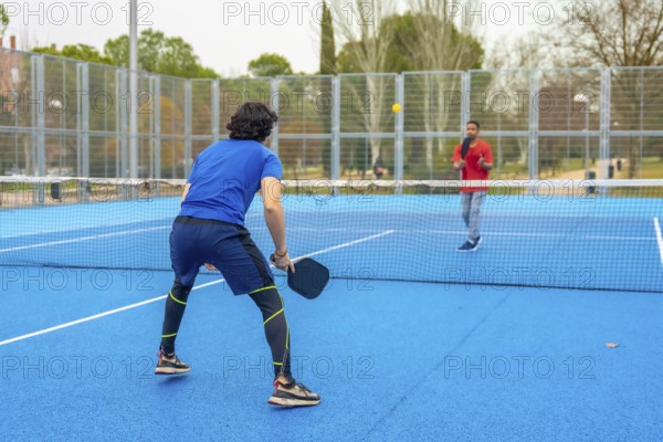 Two male athletes playing an intense pickleball game on a vibrant blue court, holding paddles and