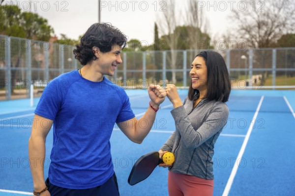 Young man and woman celebrating success with a fist bump, smiling and standing together on a bright