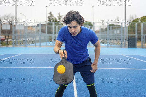 Young man in sportswear concentrating on a serve, gripping a pickleball paddle as a yellow ball