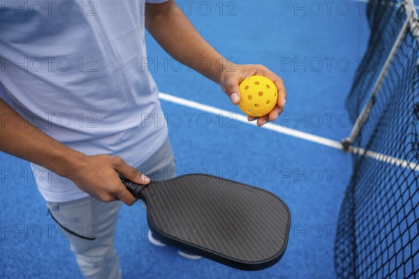 Person standing on a bright blue pickleball court, holding a black paddle and a yellow perforated