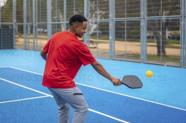 Young athletic man in sportswear striking a pickleball with a paddle on a vibrant blue outdoor