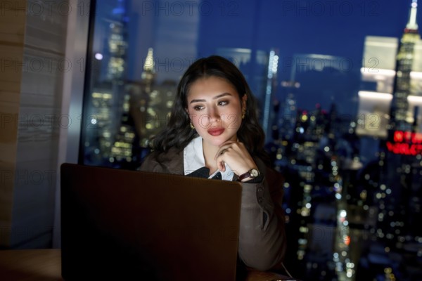 Young businesswoman working late on a laptop in a modern office, gazing toward the illuminated
