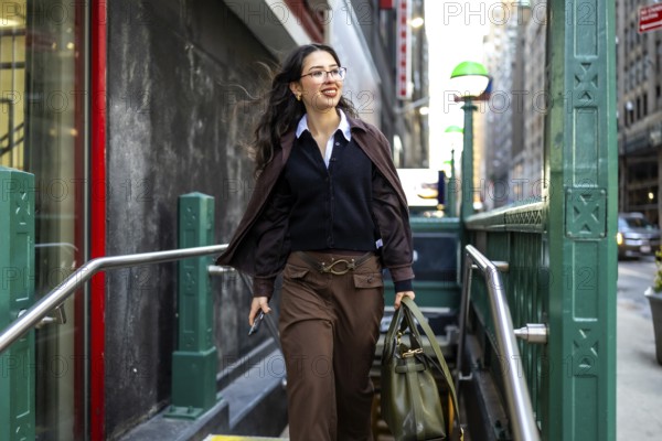 Young businesswoman with glasses and a professional bag emerging from a subway station entrance,