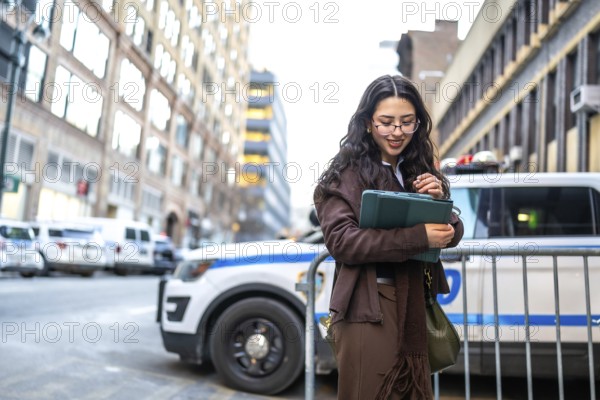 Young executive woman is holding a modern tablet and smiling, standing outdoors in a bustling city