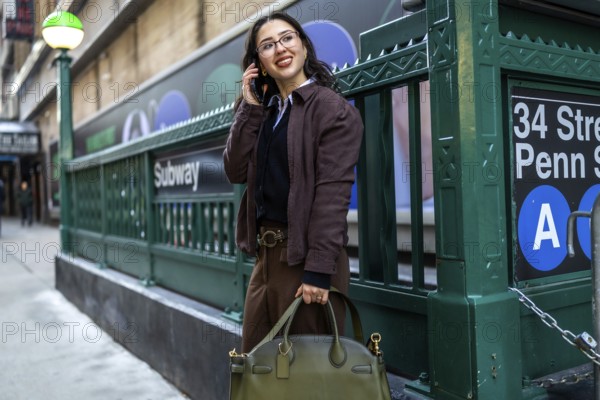 Young businesswoman smiling, talking on a mobile phone, and carrying a handbag while standing near