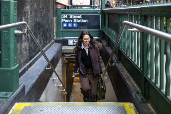 Young female executive with a satchel bag going down the stairs of the 34 street penn station a c e