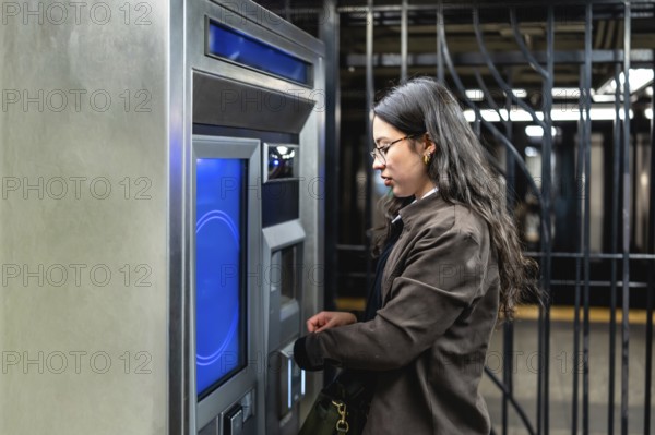 Young businesswoman with glasses and sleek dark hair interacting with a subway ticket machine,