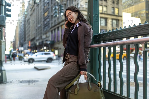 Young businesswoman smiling on a phone call, leaning against a green subway railing on a busy