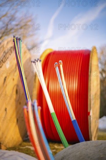 Colourful cables in a wintry environment in front of large, red cable spools, fibre-optic