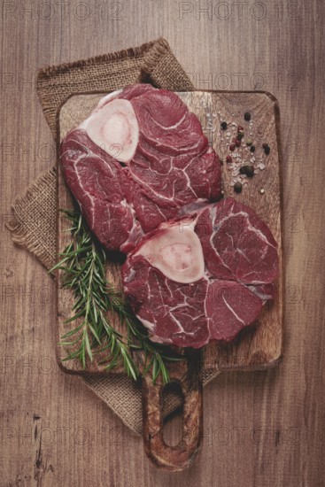 Knuckle on the bone, raw meat for ossobuco, on a wooden chopping board, with a sprig of rosemary,