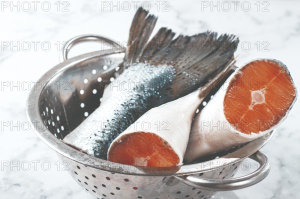 Fish tails are placed in a colander on a marble counter. The colander allows water to drain away