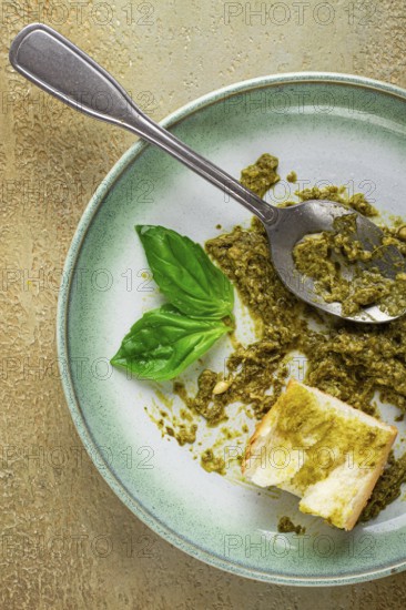 On a platter is a pesto sauce made from fresh basil, with a slice of bread and a spoon on a plate.