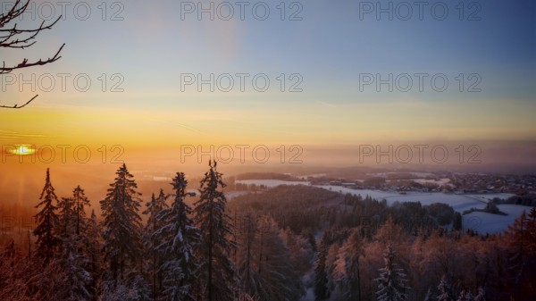 A wintry sunset over a snow-covered forest with glowing sky, Frankenwald nature park Park, Upper