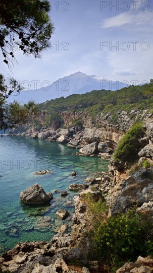 Rocky coast with clear blue water and view of snow-capped mountains in the background, view of