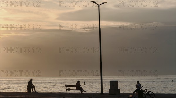 People sitting and bikers by the sea at sunset, quiet and peaceful atmosphere, waterfront, Izola,