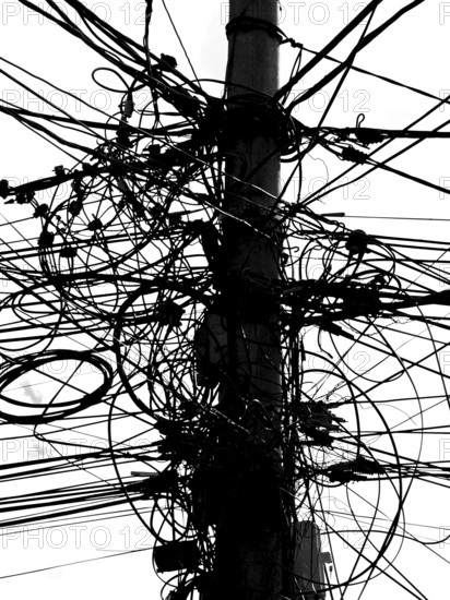 A power pole with a messy tangle of cables in an urban environment, black and white, Prizren,