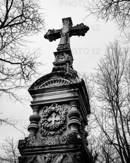 Gothic grave monument with cross in front of bare, wintery trees, black and white photograph, old