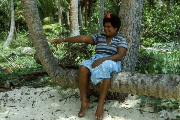 Woman sitting on a coconut trunk, (there are no chairs on Tavewa) Tavewa Island, Yasawa Islands,