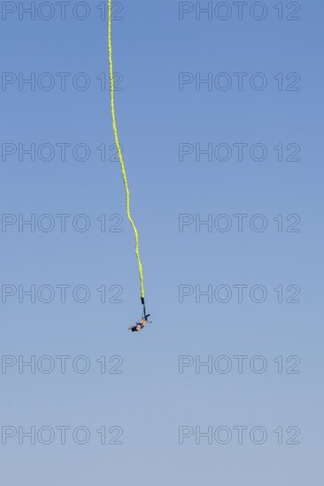 Female bungee jumper in midair with her ankles tied to a long yellow elastic bungee jumping cord,