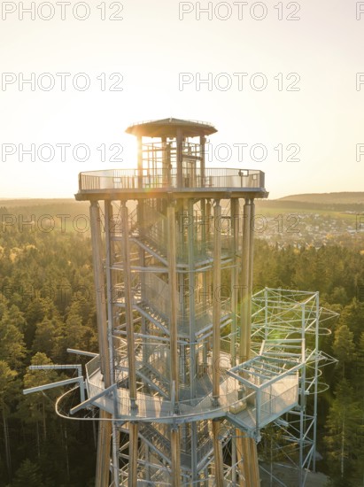 Sunbeams from an observation tower standing over a dense forest shine through the metal structure,