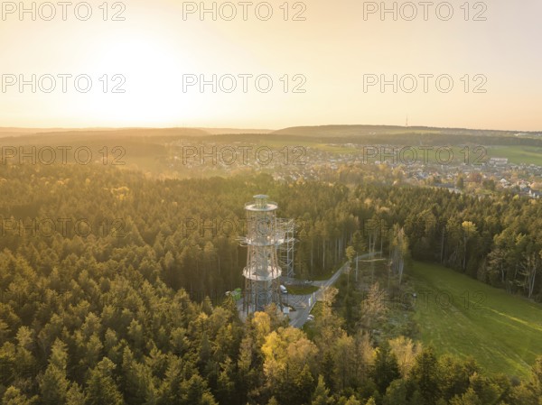 A tower towers over a forest, the view extends to a city in warm sunset light, Himmelsglück