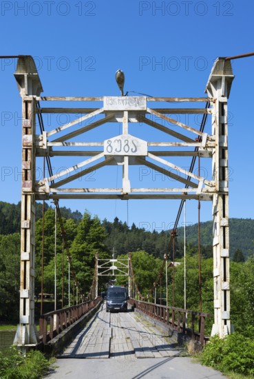 Car drives over an old suspension bridge surrounded by forest, camper, motorhome on a suspension
