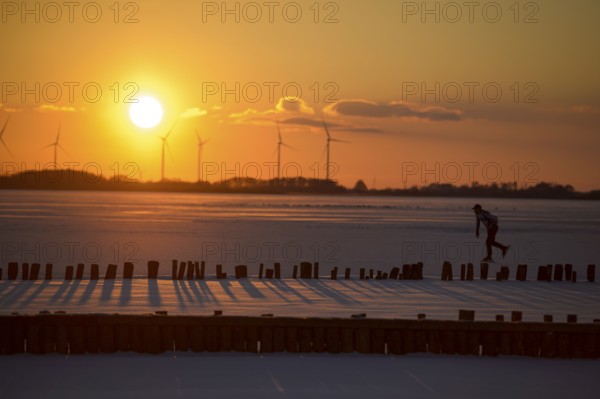 Ice skaters in front of sunset over icy landscape with wind turbines and intense colors on the
