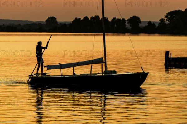 Sailing boat with person on calm Dümmer See brought into the harbor with a long stake at sunset,