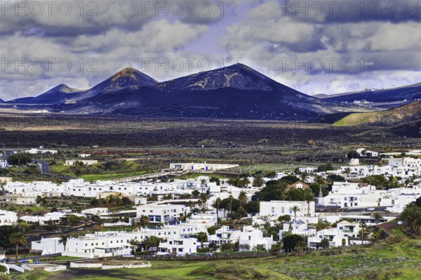 The municipality of Yaiza with white houses in a volcanic mountain landscape and cloudy sky, Yaiza