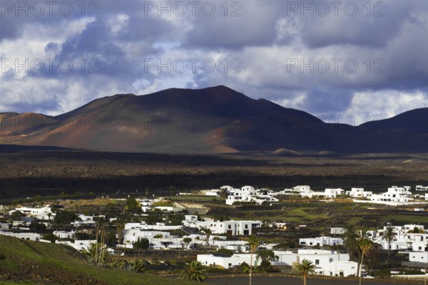 Partial view of the municipality of Yaiza at the foot of volcanic mountains under dramatic clouds