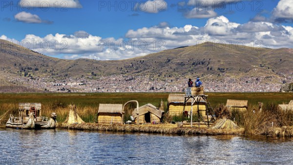Reed huts and lakeside observation tower in sunny weather with mountains in the background, The