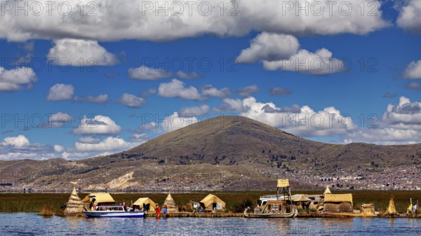 Reed village on the shore of a lake with big mountains in the background under a cloudy sky, The