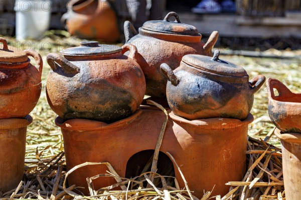 Clay pots and cooking areas arranged on a straw bed with rustic charm, The floating reed islands of