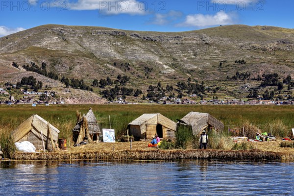 Huts on a reed island in front of a village and mountains, reflecting in the water, The floating