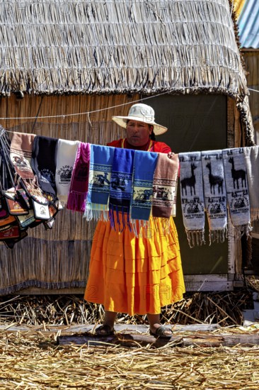 Woman showing colorful, handmade cloths in front of a thatched hut, The floating reed islands of