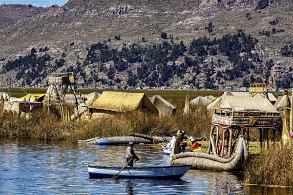 A boat sails on a lake against a backdrop of reed huts and mountains, the floating reed islands of