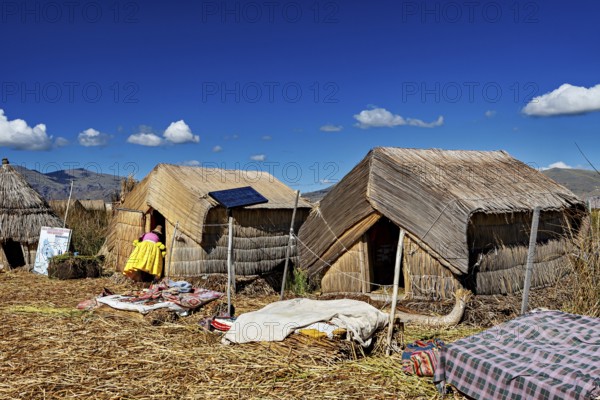 Reed huts with solar panels under a clear blue lakeside sky, The floating reed islands of the Uros