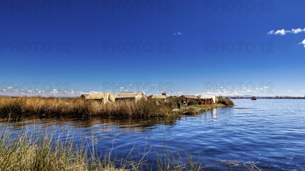 View of reed huts on the coast of a lake under expansive blue sky, The floating reed islands of the