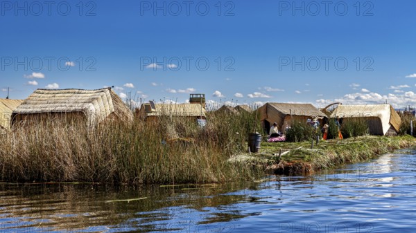 Rows of reed huts along a lake under clear blue skies, The floating reed islands of the Uros in