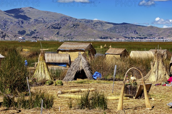 Traditional reed huts on the edge of a lake with mountains in the background, The floating reed