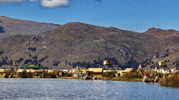 Huts on the shores of a lake in front of a mountainous landscape under a blue sky, The floating