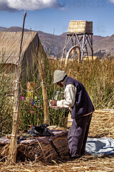 Man is engaged in handicraft work next to traditional reed huts, the floating reed islands of the