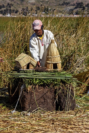 Man showing a model of straw huts and figures on a natural surface, The floating reed islands of