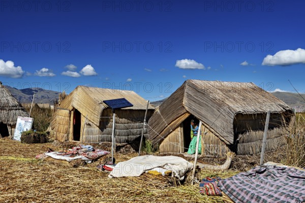 Several reed huts with solar panels under a blue lakeside sky, The floating reed islands of the