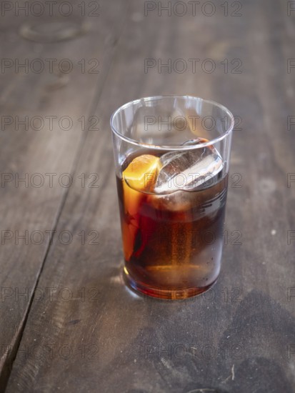 Glass of dark alcoholic cocktail with ice and orange zest on a rustic wooden table