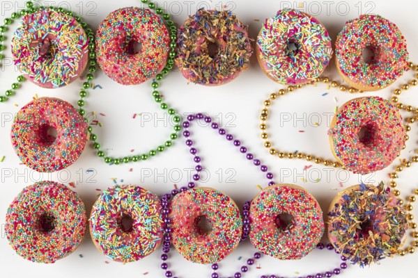 Donuts with colorful icing and sprinkles surrounded by colored pearl necklaces on a white