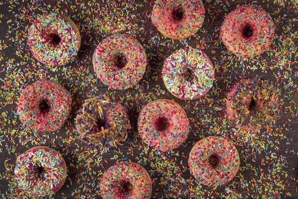Donuts with sprinkles on wooden table, colorful ornaments scattered