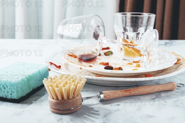 Dishes are stacked on a kitchen counter with food remnants after a meal. A cleaning brush and