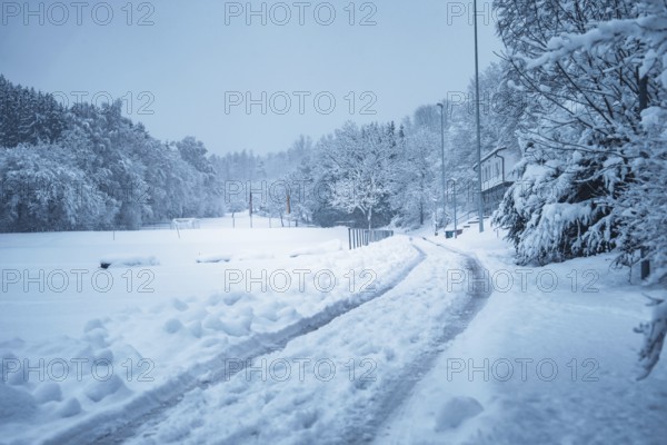 A snowy road leads through a wintry landscape with trees and houses, Besenfeld, Black Forest,
